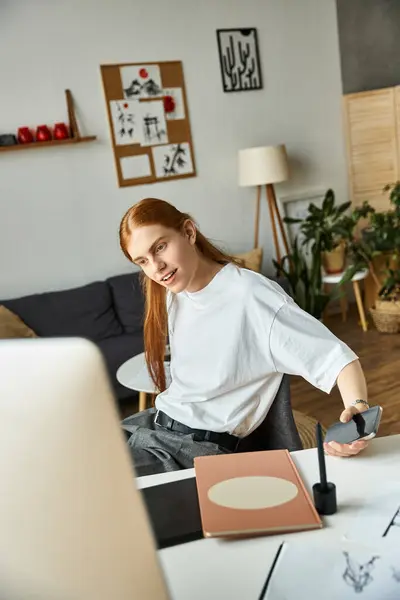 A young man with long red hair smiles during a video chat at his stylish home office. — Stock Photo