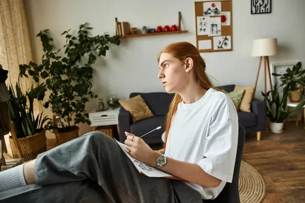 A focused young man sits thoughtfully, sketching in a comfortable living area filled with greenery. — Stock Photo