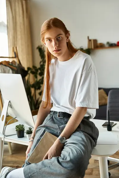 A young man rests on a desk, clutching a book, lost in thought in a warm and inviting room. — Stock Photo