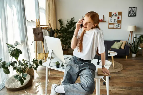 Um jovem conversa entusiasticamente ao telefone enquanto está sentado em um espaço de trabalho moderno e bem iluminado. — Fotografia de Stock