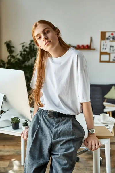 A young man leans against a desk in a bright, stylish office filled with greenery. — Stock Photo