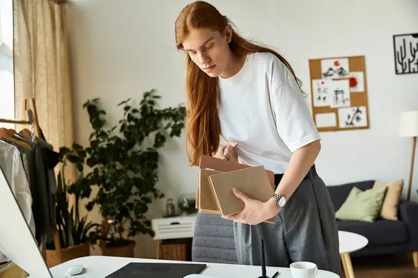 A young man carefully sorts through notebooks in a modern, inviting home office setting. — Stock Photo