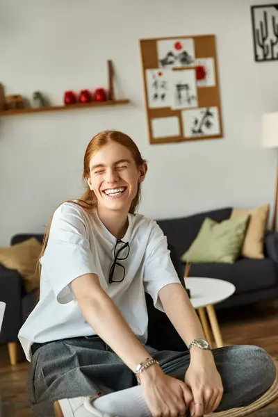 Un joven se sienta con una expresión alegre, irradiando felicidad en un espacio acogedor. - foto de stock
