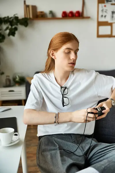 A young man with long hair enjoys a moment of leisure while using an electronic device. — Stock Photo