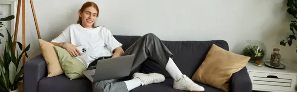 A young man enjoys leisure time lounging on a comfortable sofa with a laptop. — Stock Photo