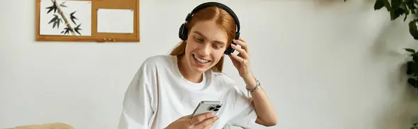 A young man smiles while listening to music on his phone, feeling relaxed at home. — Stock Photo