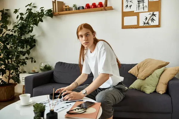 A young man with long hair focuses intently on his creative project while seated comfortably. — Stock Photo