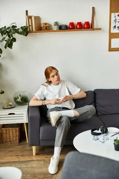In a calm room, a young man sits on a couch, lost in thought amid the decor. — Stock Photo