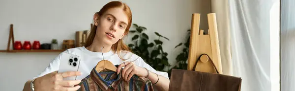Молодой человек держит красочную одежду, делая селфи в современном, ярком пространстве. — стоковое фото