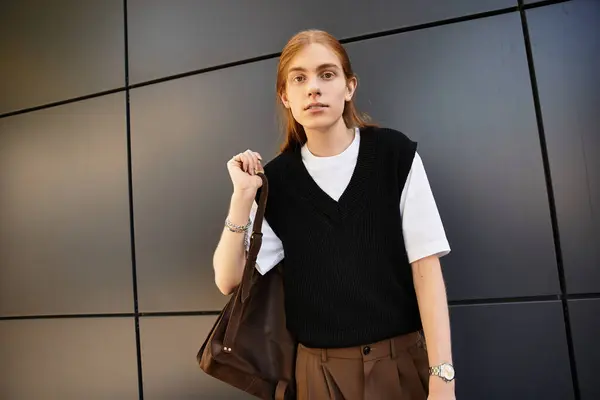 The young man stands confidently, holding a bag while showcasing his trendy attire. — Stock Photo