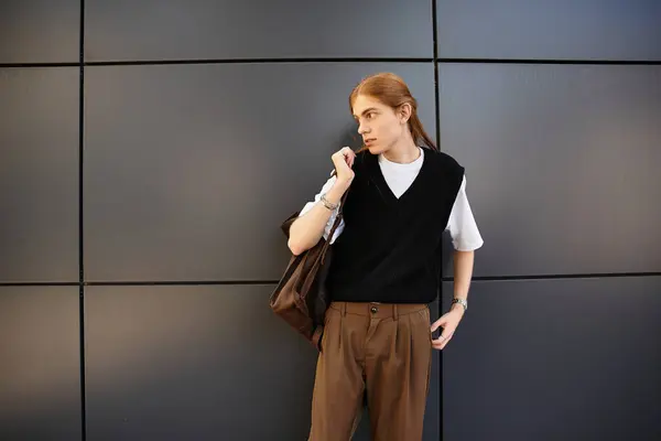 The young man stands confidently dressed in a trendy outfit while holding a bag. — Stock Photo