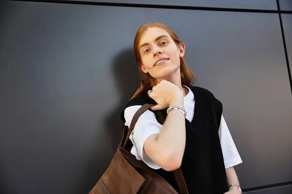 A young man showcases his casual style while holding a bag, smiling in an urban setting. — Stock Photo
