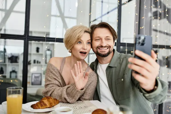 A loving couple enjoys breakfast together while taking a joyful selfie at home. — Stock Photo