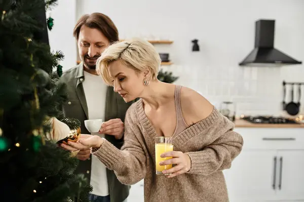 A loving couple enjoys decorating their Christmas tree with ornaments and holiday cheer at home. — Stock Photo