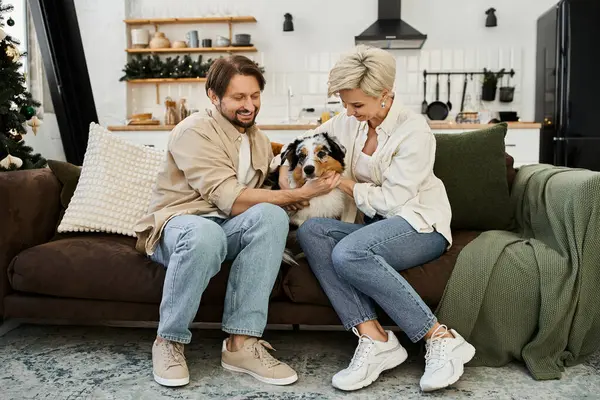 A happy couple enjoys quality time together on their couch, petting their dog in a cozy home. — Stock Photo
