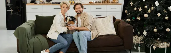 Um casal se senta no sofá, cercado por decorações de férias e seu cão amado. — Fotografia de Stock
