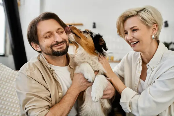 A happy couple shares laughter and affection while their dog playfully licks the man. — Stock Photo