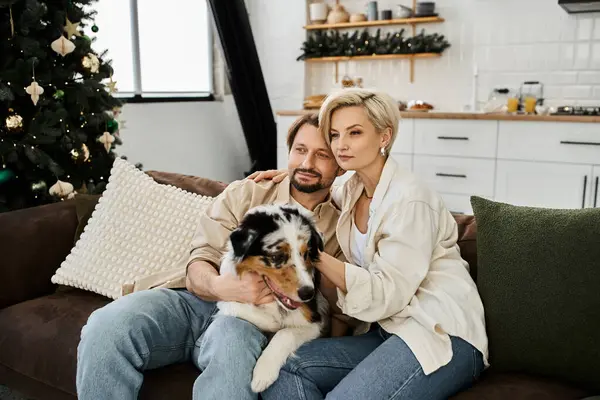 A couple relaxes on their couch, surrounded by holiday decorations, while cuddling their dog. — Stock Photo
