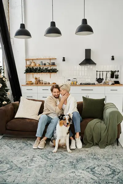 A couple sits closely on a comfy couch, sharing affection while their dog watches happily. — Stock Photo