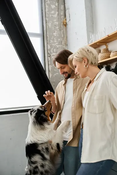 The couple shares joyful interactions with their furry friend in a cozy, sunlit room. — Stock Photo