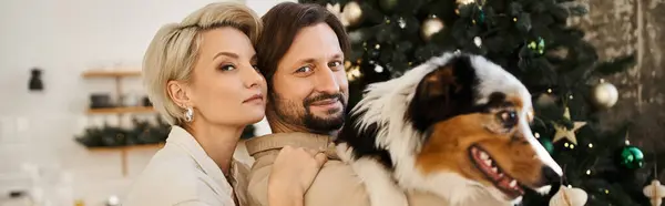 A couple enjoys a loving moment with their dog in a cozy, holiday decorated home. — Stock Photo
