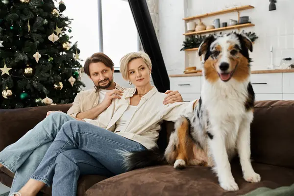 A couple relaxes together on a sofa, sharing warmth and smiles while their dog sits happily nearby. — Stock Photo
