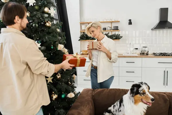 A loving couple shares a tender moment exchanging gifts by a beautifully decorated tree. — Stock Photo