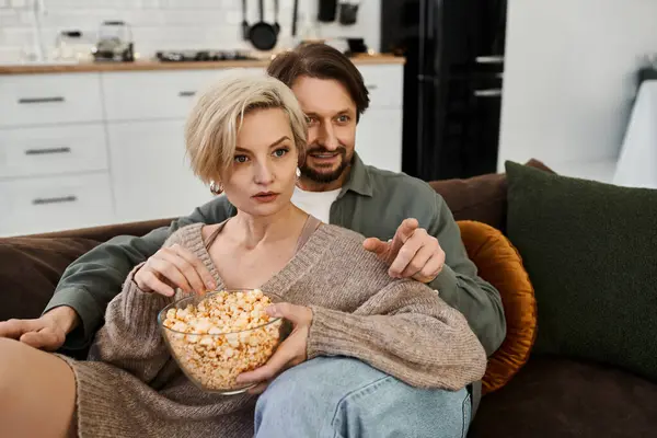 A couple shares a tender moment on the couch, enjoying popcorn and a movie night at home. — Stock Photo