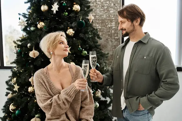 A couple enjoys sparkling drinks together while sitting by their festive Christmas tree. — Stock Photo