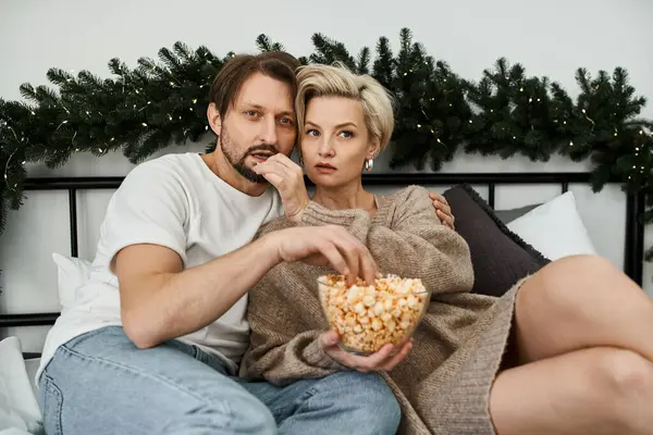 A couple sits closely together on their bed, sharing laughter and popcorn while relaxing. — Stock Photo