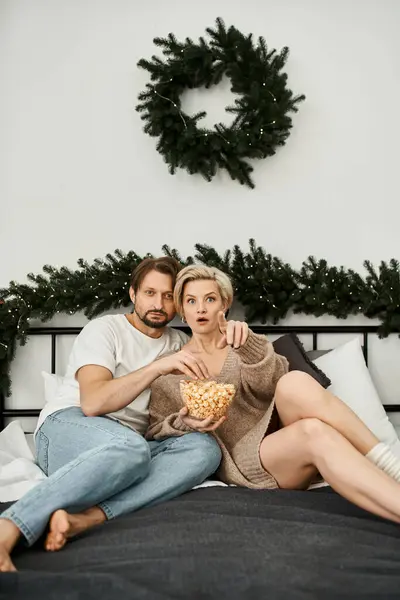 Un couple sucré aime le pop-corn sur son lit, entouré de décorations chaudes de vacances et de rires. — Photo de stock