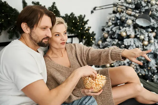 Ein Paar entspannt sich zu Hause und teilt sich eine Schüssel Popcorn, während man gemeinsam etwas anschaut. — Stockfoto