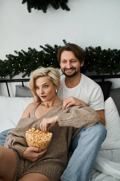 Un couple s'assoit ensemble sur leur lit, partageant du pop-corn et souriant dans une ambiance cosy. — Photo de stock