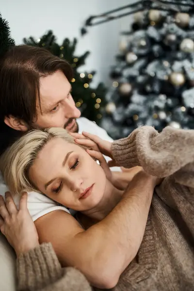 A couple enjoys a tender embrace on a cozy couch surrounded by festive decorations. — Stock Photo