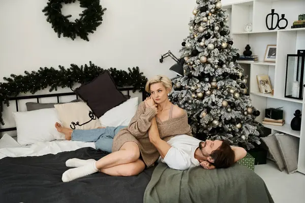 Una pareja amorosa disfruta de un momento tranquilo juntos en una cama en una acogedora habitación adornada para las vacaciones. - foto de stock
