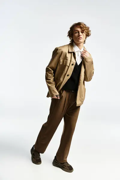 A handsome young man in a chic autumn outfit poses confidently in a minimalist studio space. — Fotografia de Stock