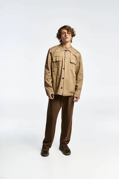 A handsome young man with wavy hair models a chic autumn outfit in a contemporary studio space. — Stock Photo
