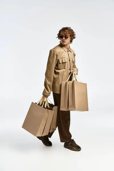 A handsome young man in a chic autumn outfit confidently carries shopping bags in a modern studio setting. — Stock Photo