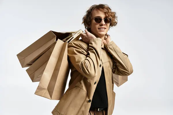 A dapper young man displays his elegant autumn attire while holding shopping bags in a studio. — Stock Photo