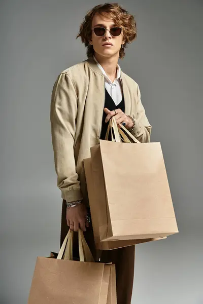 A handsome young man in an elegant autumn outfit poses confidently with shopping bags in a studio. — Stock Photo