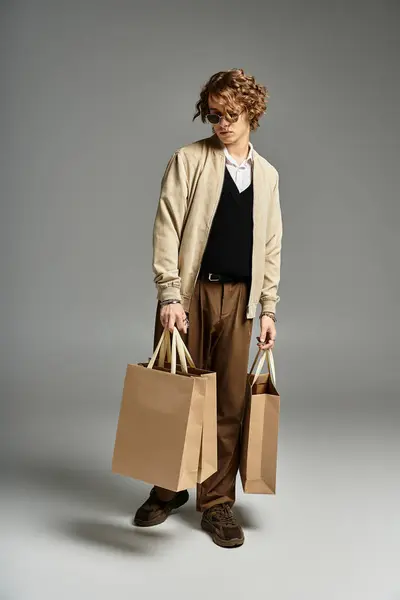 A handsome young man in an elegant autumn outfit holds shopping bags while posing in a stylish studio. — Stock Photo
