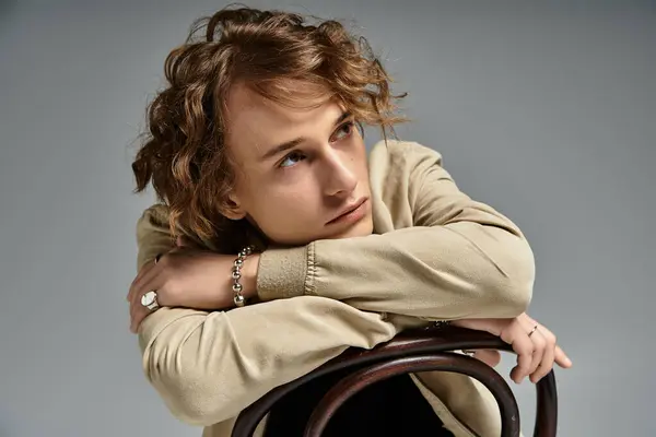 Un bel giovane uomo in un vestito alla moda autunno si appoggia su una sedia, trasudando fascino e raffinatezza. — Foto stock