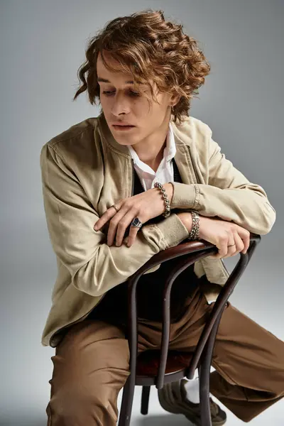 A handsome young man sits thoughtfully on a chair, dressed in elegant autumn fashion and showcasing his wavy hair. — Stock Photo