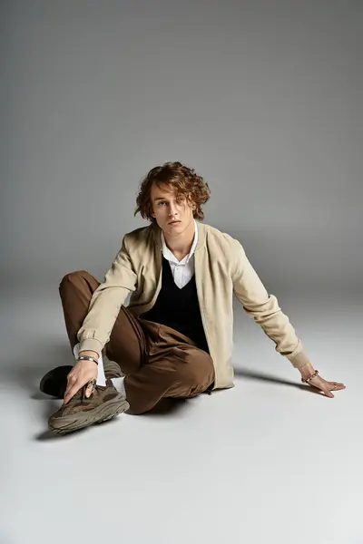 This young man with wavy hair elegantly poses in autumn attire within a contemporary studio. — Stock Photo