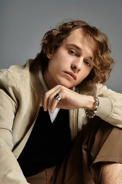 A stylish young man with wavy hair poses elegantly in a trendy autumn ensemble, emanating charm. — Stock Photo