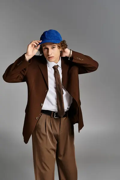 A stylish young man in a brown suit and blue cap adjusts his hat while posing in a contemporary studio. — Stock Photo