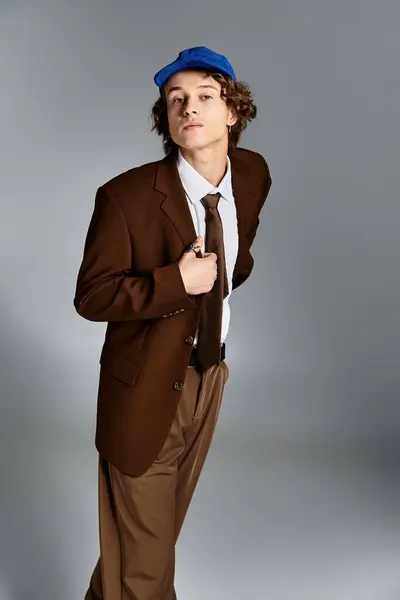 A young man dressed in a brown suit and cap confidently poses against a sleek studio backdrop. — Stock Photo