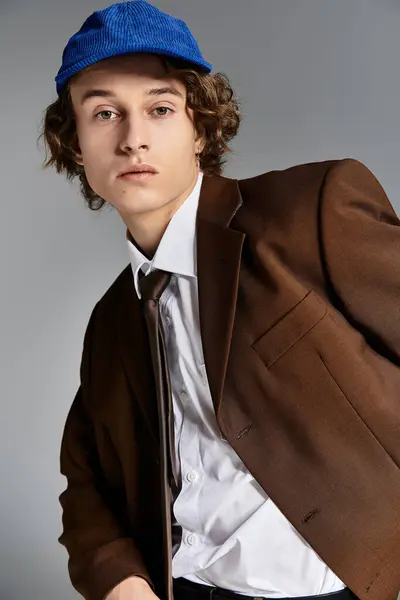 En un estudio elegante, un joven guapo vestido con un traje marrón y gorra de béisbol muestra una estética moderna. - foto de stock
