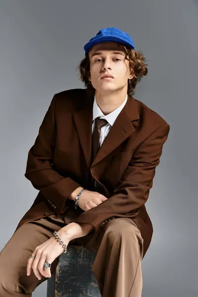 A charming young man dressed in a brown suit and baseball cap sits confidently, showcasing style and flair. — Stock Photo