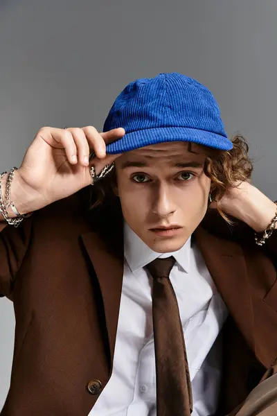 A handsome young man wearing a brown suit and blue cap strikes a contemplative pose in a studio space. — Stock Photo